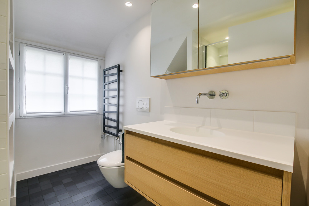 Mid-sized eclectic master bathroom in Paris with light wood cabinets, a curbless shower, a wall-mount toilet, white tile, porcelain tile, white walls, ceramic floors, an undermount sink, solid surface benchtops, black floor and an open shower.