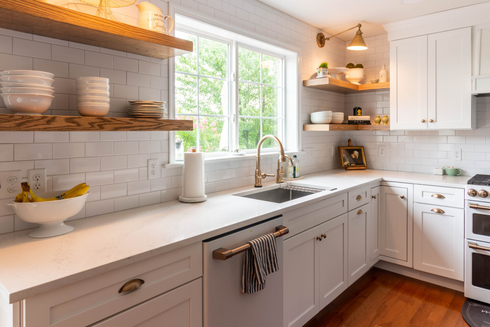 Mid-sized transitional l-shaped medium tone wood floor and brown floor open concept kitchen photo with an undermount sink, shaker cabinets, white cabinets, quartzite countertops, white backsplash, ceramic backsplash, white appliances, an island and white countertops