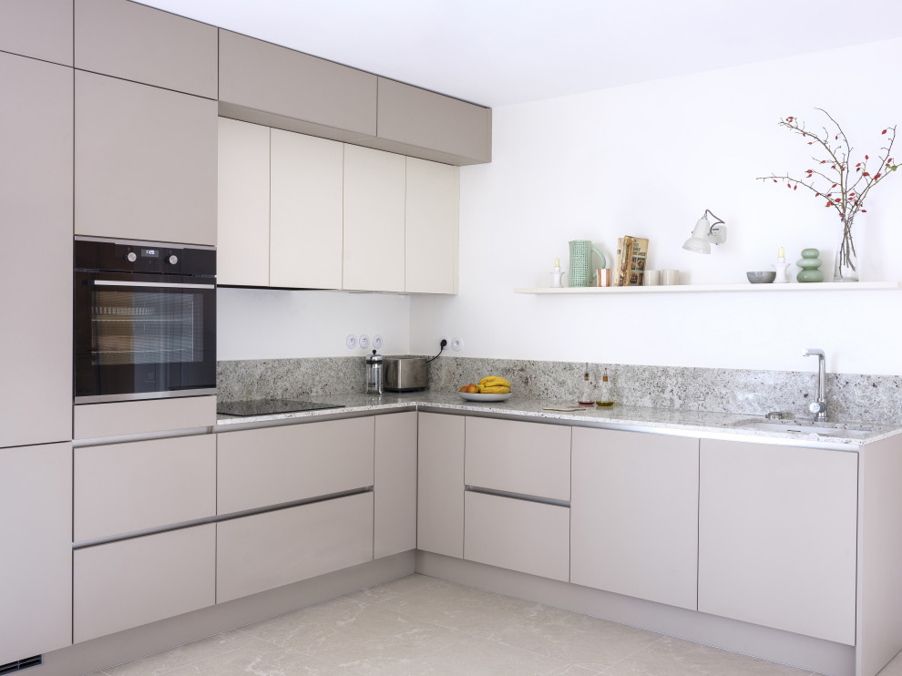 Photo of a large modern l-shaped open plan kitchen in Paris with a double-bowl sink, flat-panel cabinets, beige cabinets, granite benchtops, grey splashback, granite splashback, panelled appliances, ceramic floors and beige floor.