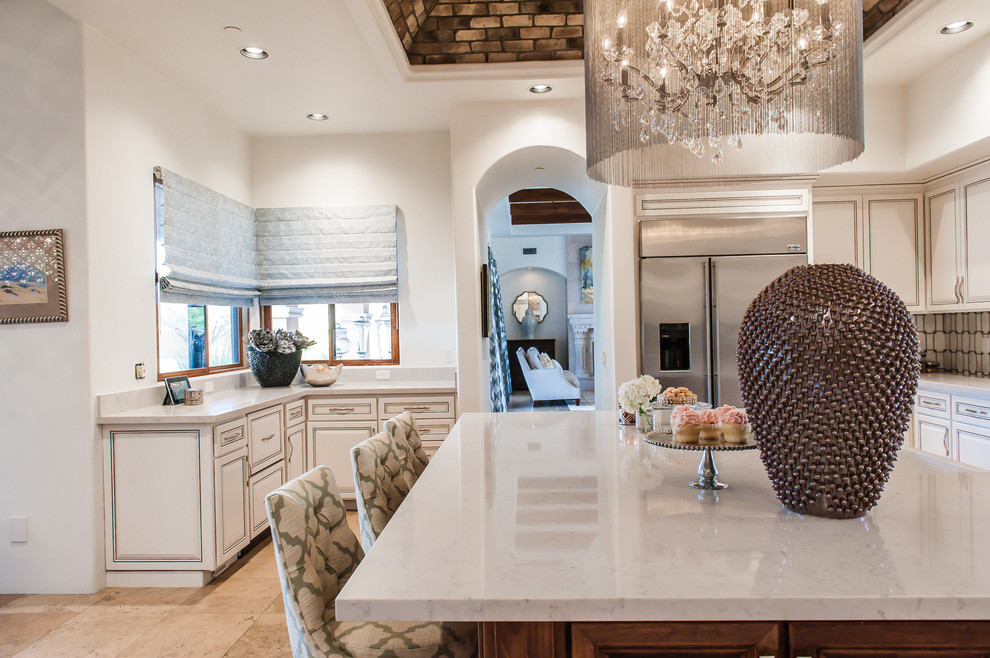 Large transitional single-wall travertine floor open concept kitchen photo in Phoenix with a farmhouse sink, raised-panel cabinets, white cabinets, marble countertops, white backsplash, stone tile backsplash, stainless steel appliances and an island