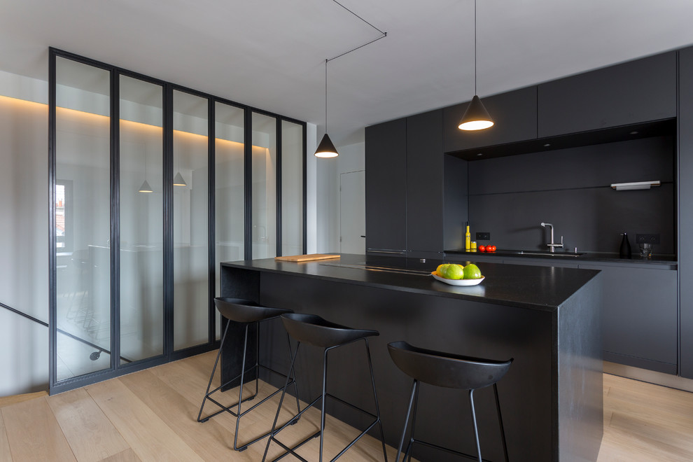 Inspiration for a mid-sized contemporary galley open plan kitchen in Paris with an integrated sink, flat-panel cabinets, black cabinets, granite benchtops, black splashback, stainless steel appliances, light hardwood floors and with island.
