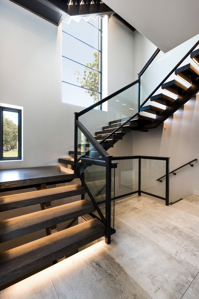 This is an example of a mid-sized modern wood u-shaped staircase in Dallas with open risers and glass railing.