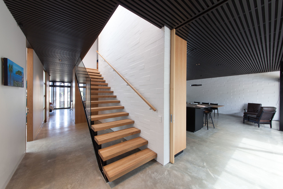 Large modern wood straight staircase in Auckland with open risers and glass railing.