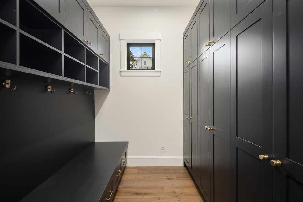Design ideas for a mid-sized country galley dedicated laundry room in Seattle with shaker cabinets, black cabinets, white walls, medium hardwood floors and brown floor.
