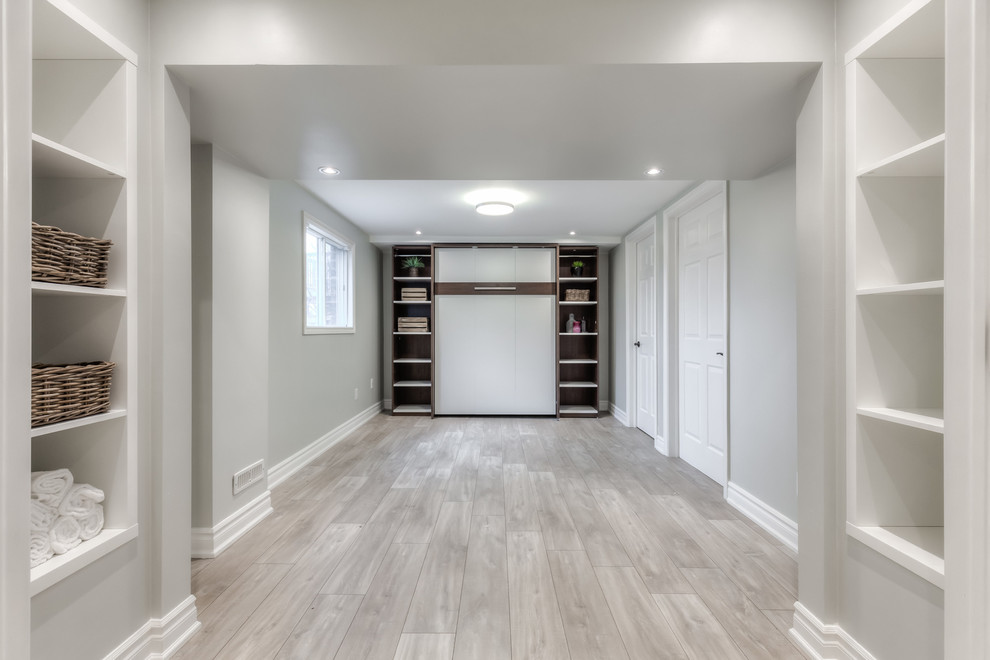 This is an example of a small beach style walk-out basement in Toronto with white walls and laminate floors.