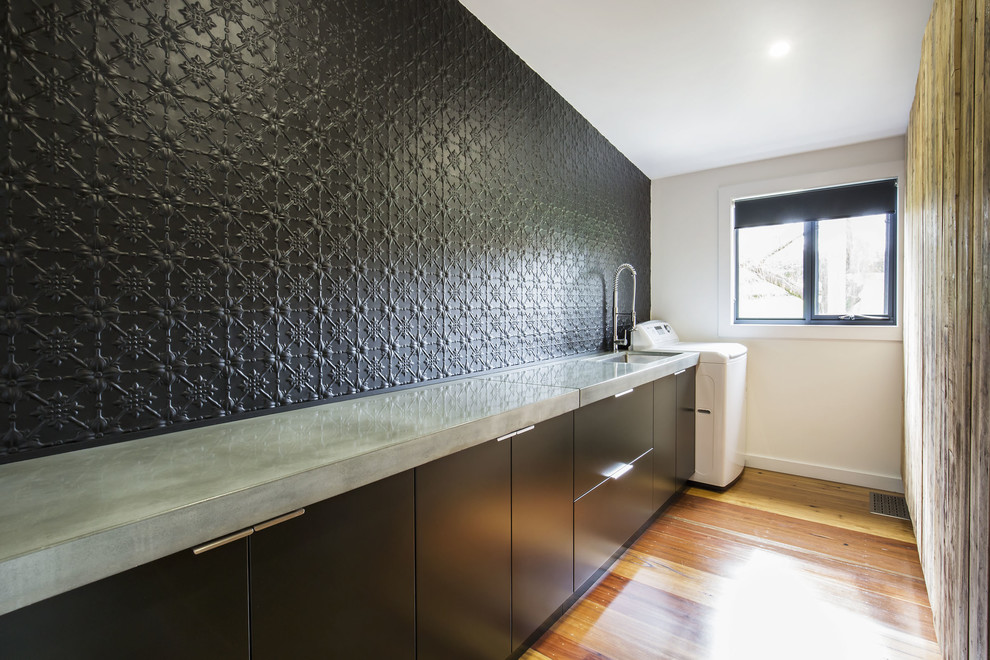 Mid-sized contemporary galley utility room in Sydney with an undermount sink, flat-panel cabinets, black cabinets, concrete benchtops, black walls and medium hardwood floors.