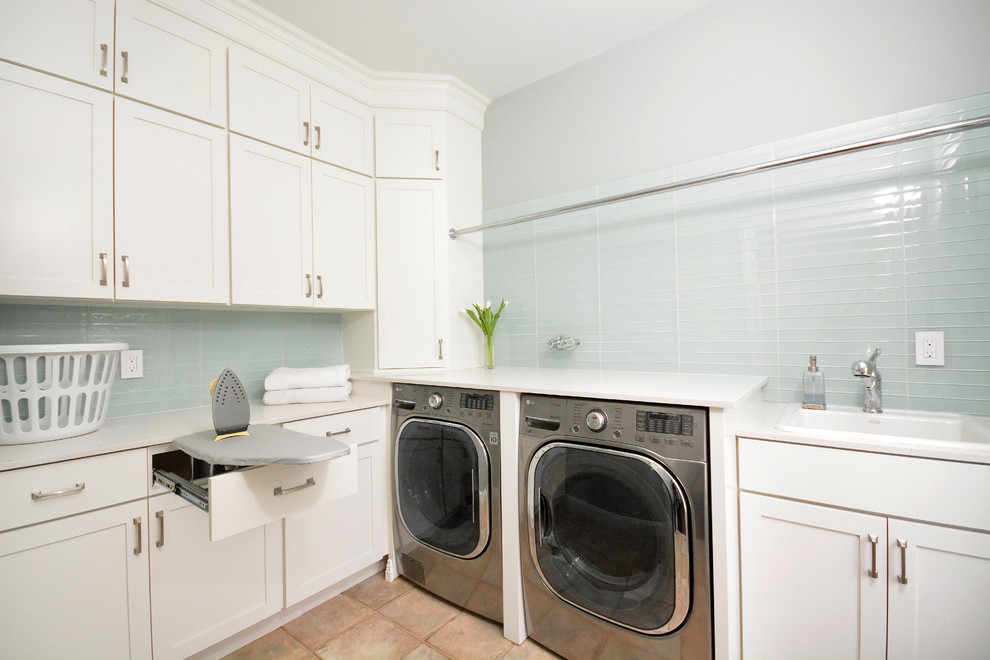This is an example of a mid-sized transitional l-shaped dedicated laundry room in New York with a drop-in sink, recessed-panel cabinets, white cabinets, quartz benchtops, terra-cotta floors, a side-by-side washer and dryer and grey walls.
