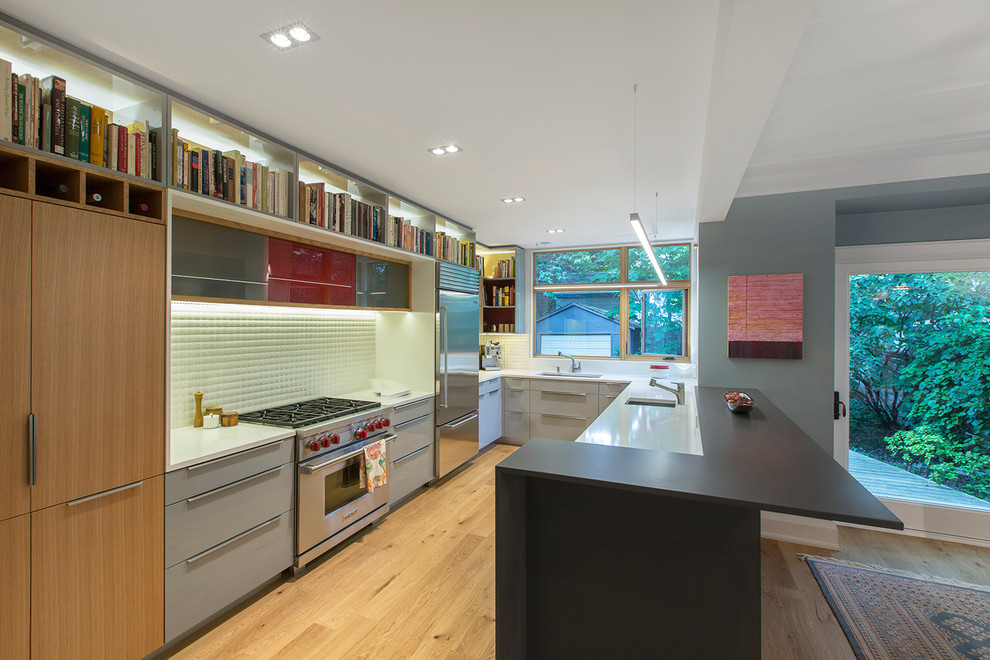 Photo of a mid-sized contemporary u-shaped eat-in kitchen in Toronto with an undermount sink, flat-panel cabinets, grey cabinets, quartz benchtops, white splashback, porcelain splashback, stainless steel appliances, light hardwood floors and a peninsula.
