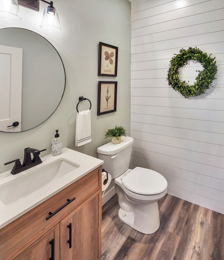 This is an example of a mid-sized country bathroom in Other with shaker cabinets, medium wood cabinets, a two-piece toilet, white walls, vinyl floors, a console sink, multi-coloured floor, white benchtops, a single vanity, a freestanding vanity and planked wall panelling.