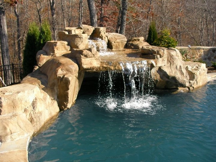 Large tropical backyard custom-shaped pool in Charlotte with a water feature and natural stone pavers.