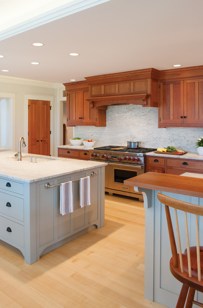 Inspiration for an arts and crafts single-wall eat-in kitchen in Portland Maine with a single-bowl sink, shaker cabinets, medium wood cabinets, granite benchtops, white splashback, stone slab splashback, stainless steel appliances, light hardwood floors and multiple islands.