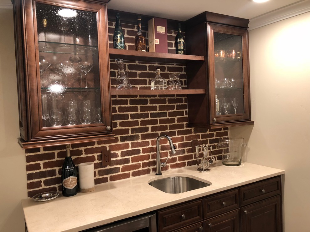 This is an example of a large traditional single-wall seated home bar in Denver with an undermount sink, glass-front cabinets, dark wood cabinets, quartz benchtops, red splashback and brick splashback.