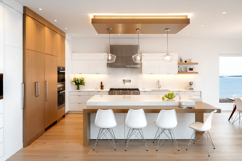 Contemporary l-shaped eat-in kitchen in Other with an undermount sink, flat-panel cabinets, medium wood cabinets, white splashback, panelled appliances, medium hardwood floors, with island, brown floor, white benchtop and recessed.