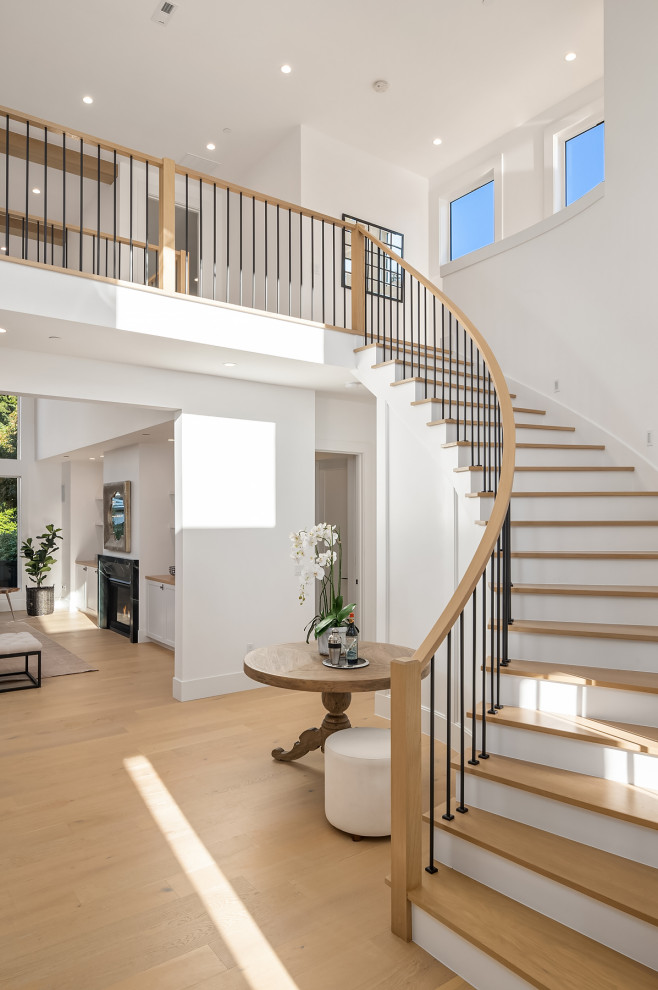 Стильный дизайн: большая изогнутая лестница в современном стиле с деревянными ступенями, крашенными деревянными подступенками, перилами из смешанных материалов и панелями на части стены - последний тренд