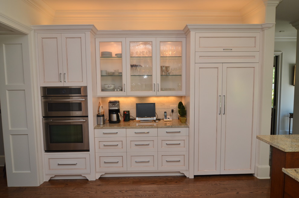 Inspiration for a mid-sized transitional u-shaped medium tone wood floor kitchen remodel in Orlando with a drop-in sink, raised-panel cabinets, white cabinets, granite countertops, beige backsplash, stone slab backsplash, stainless steel appliances and an island