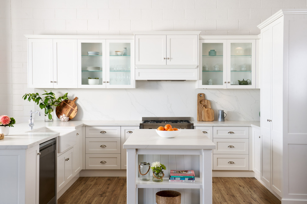 Inspiration for a transitional u-shaped kitchen in Perth with a farmhouse sink, shaker cabinets, white cabinets, stainless steel appliances, medium hardwood floors, with island, brown floor and white benchtop.