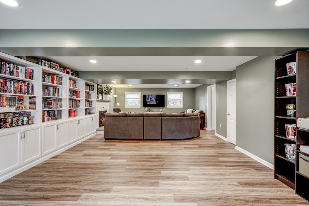 This is an example of a large arts and crafts walk-out basement in Other with green walls, vinyl floors, a standard fireplace, a brick fireplace surround and brown floor.