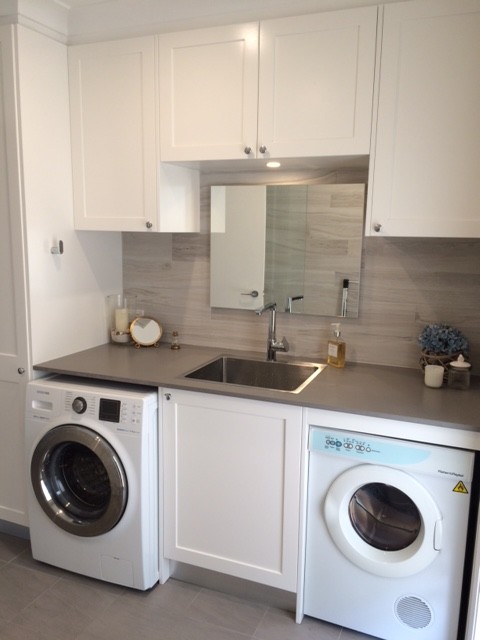Photo of a small modern single-wall utility room in Sydney with a drop-in sink, recessed-panel cabinets, white cabinets, quartz benchtops, grey walls, porcelain floors and a side-by-side washer and dryer.