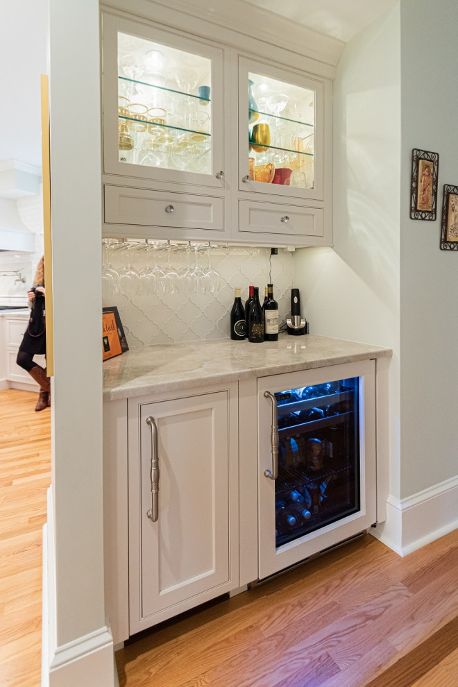 Photo of a small transitional single-wall home bar in Philadelphia with beaded inset cabinets, white cabinets, quartzite benchtops, white splashback, glass tile splashback, medium hardwood floors, brown floor and white benchtop.