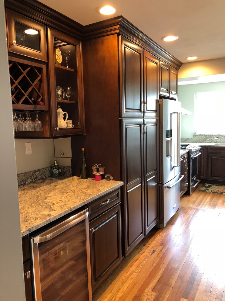 Example of a mid-sized classic l-shaped light wood floor and brown floor eat-in kitchen design with an undermount sink, raised-panel cabinets, dark wood cabinets, granite countertops, multicolored backsplash, ceramic backsplash, stainless steel appliances, an island and multicolored countertops