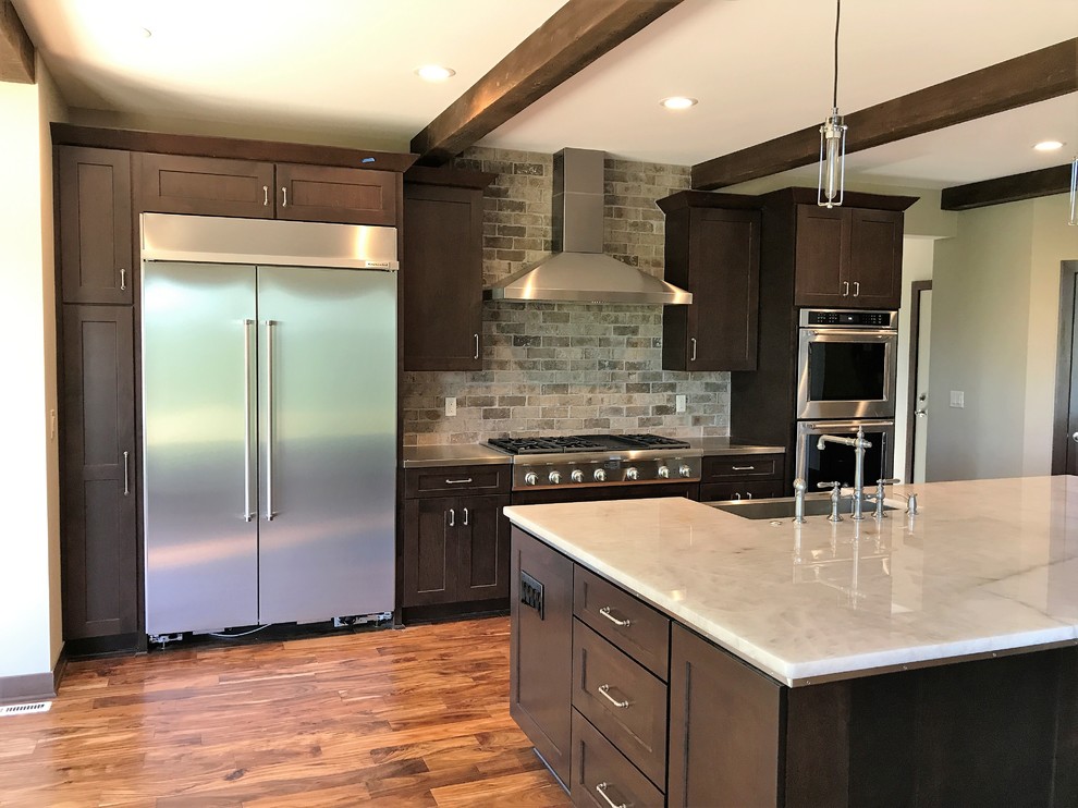 Design ideas for a large transitional single-wall open plan kitchen in Milwaukee with a farmhouse sink, shaker cabinets, dark wood cabinets, grey splashback, stainless steel appliances, dark hardwood floors, with island, brown floor, onyx benchtops and brick splashback.