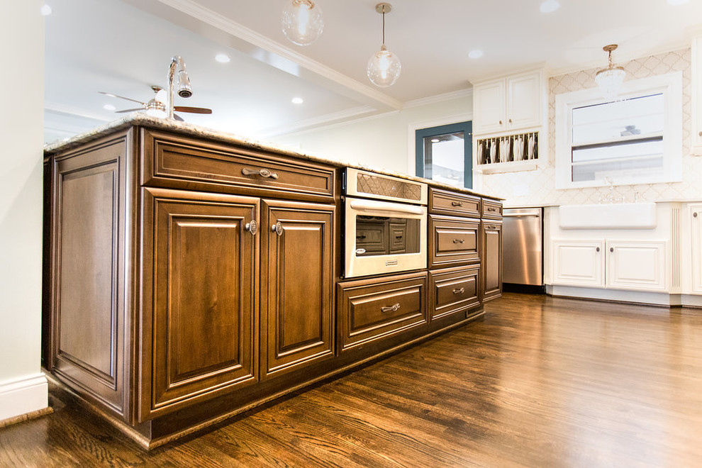 Example of a large l-shaped medium tone wood floor open concept kitchen design in Birmingham with a farmhouse sink, raised-panel cabinets, medium tone wood cabinets, granite countertops, white backsplash, ceramic backsplash, stainless steel appliances and an island