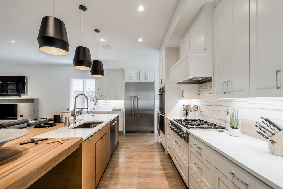 This is an example of a large contemporary l-shaped open plan kitchen in Dallas with an undermount sink, shaker cabinets, white cabinets, multi-coloured splashback, stainless steel appliances, medium hardwood floors, with island and white benchtop.
