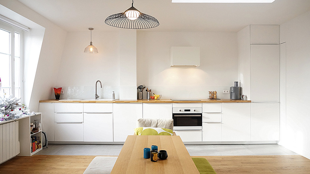 This is an example of a mid-sized contemporary single-wall open plan kitchen in Paris with a drop-in sink, white cabinets, wood benchtops, white splashback, panelled appliances and ceramic floors.