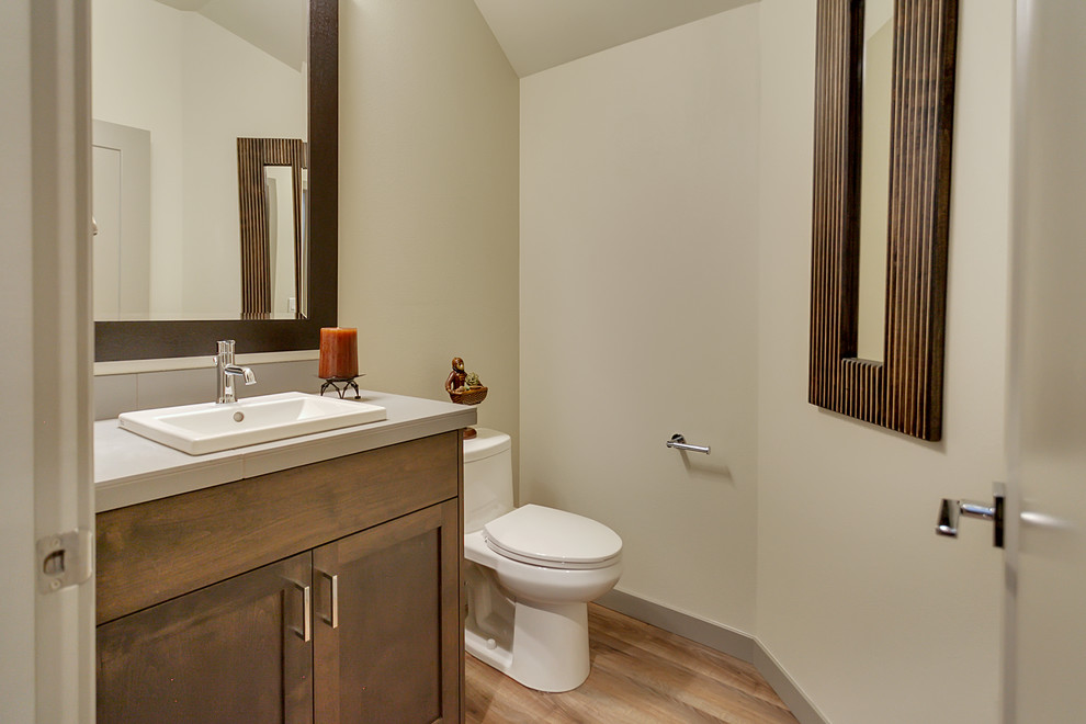 Photo of a mid-sized transitional powder room in Portland with shaker cabinets, medium wood cabinets, gray tile, ceramic tile, grey walls, medium hardwood floors, a drop-in sink, tile benchtops and a one-piece toilet.