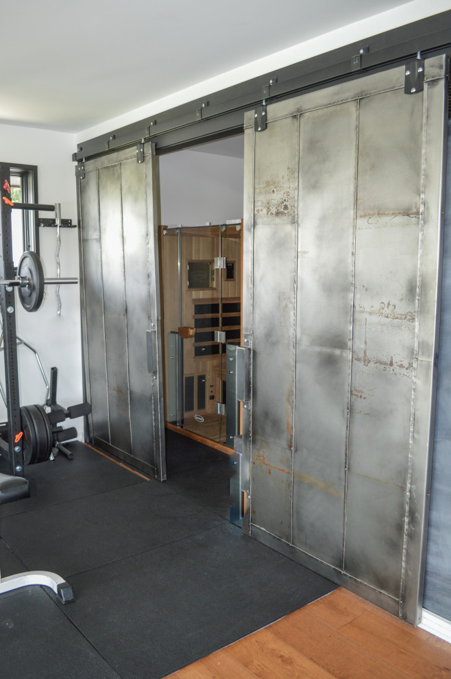 This is an example of a mid-sized industrial home weight room in Cleveland with white walls, medium hardwood floors and brown floor.
