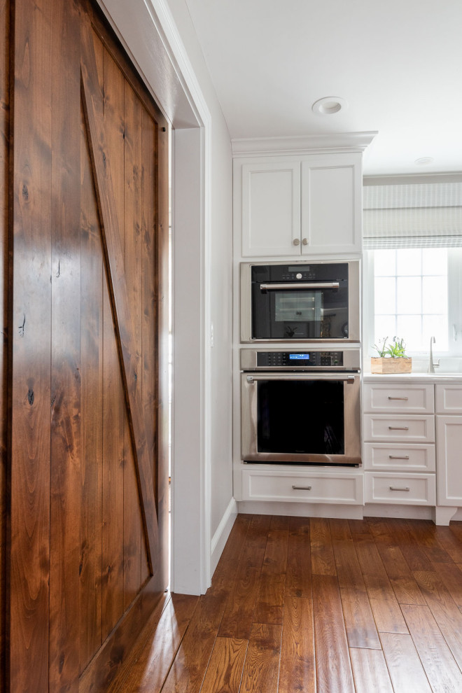 Eat-in kitchen - large transitional l-shaped medium tone wood floor and brown floor eat-in kitchen idea in Boston with an undermount sink, shaker cabinets, white cabinets, quartz countertops, white backsplash, subway tile backsplash, stainless steel appliances, an island and white countertops