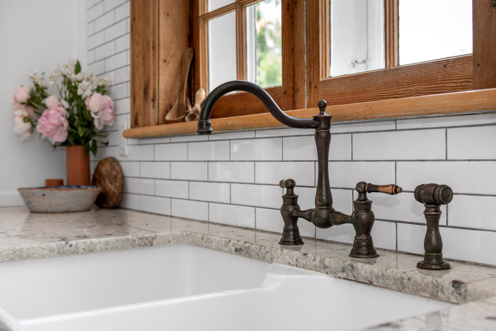 Example of a small transitional galley light wood floor and brown floor enclosed kitchen design in Ottawa with a farmhouse sink, shaker cabinets, white cabinets, granite countertops, white backsplash, subway tile backsplash, stainless steel appliances, an island and gray countertops
