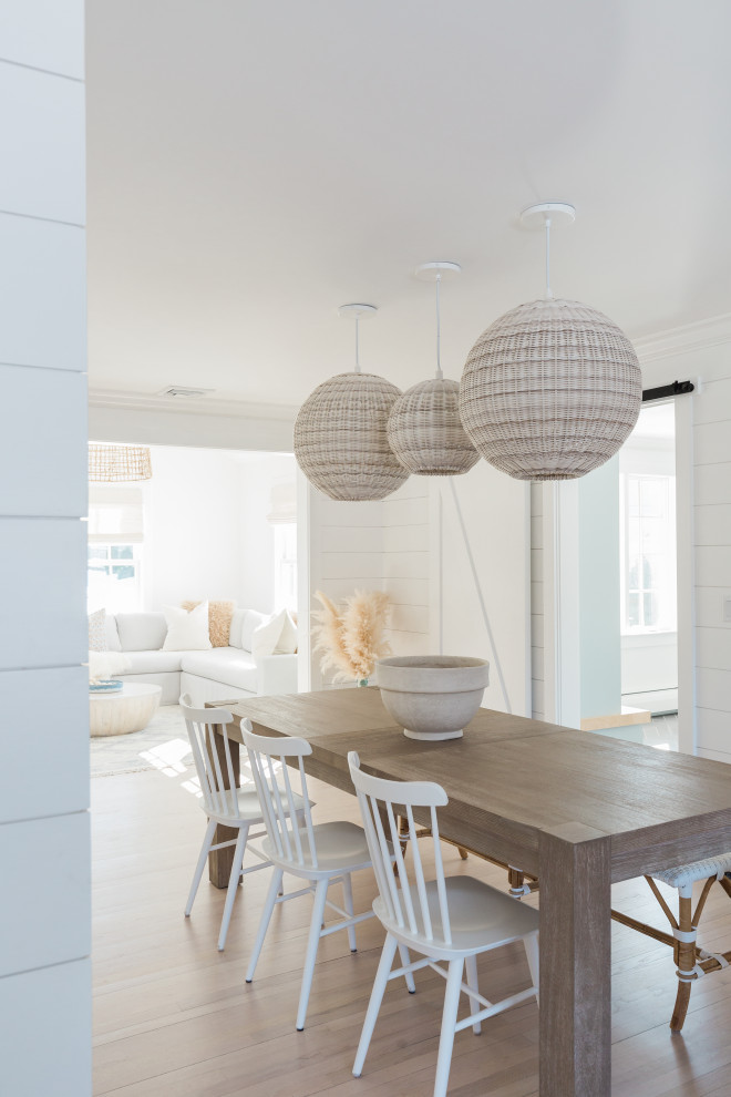 Immagine di una grande sala da pranzo aperta verso la cucina costiera con pareti bianche, parquet chiaro, pavimento beige e pareti in perlinato
