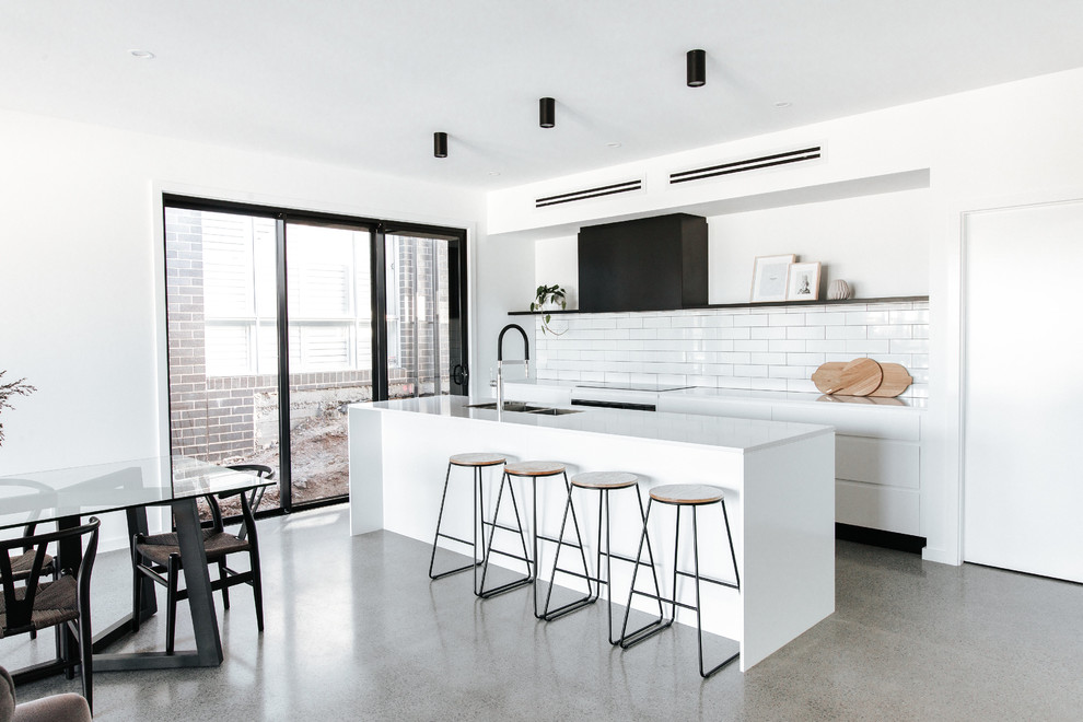 Inspiration for a mid-sized modern galley kitchen in Wollongong with a double-bowl sink, flat-panel cabinets, white cabinets, quartz benchtops, white splashback, ceramic splashback, stainless steel appliances, concrete floors, with island, grey floor and white benchtop.