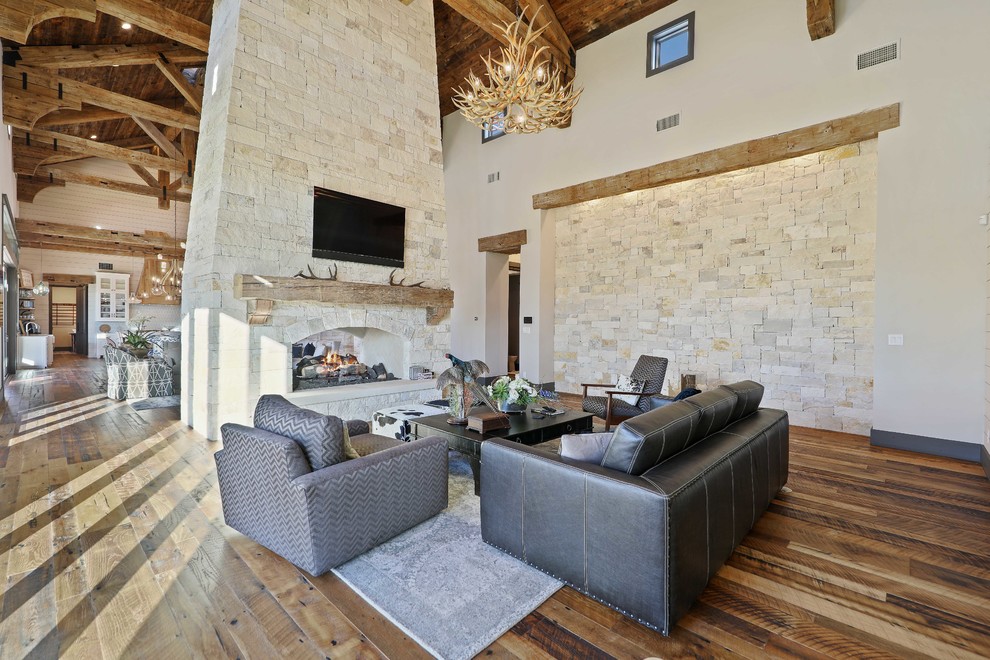 Design ideas for a country open concept living room in Austin with beige walls, medium hardwood floors, a two-sided fireplace, a stone fireplace surround and brown floor.