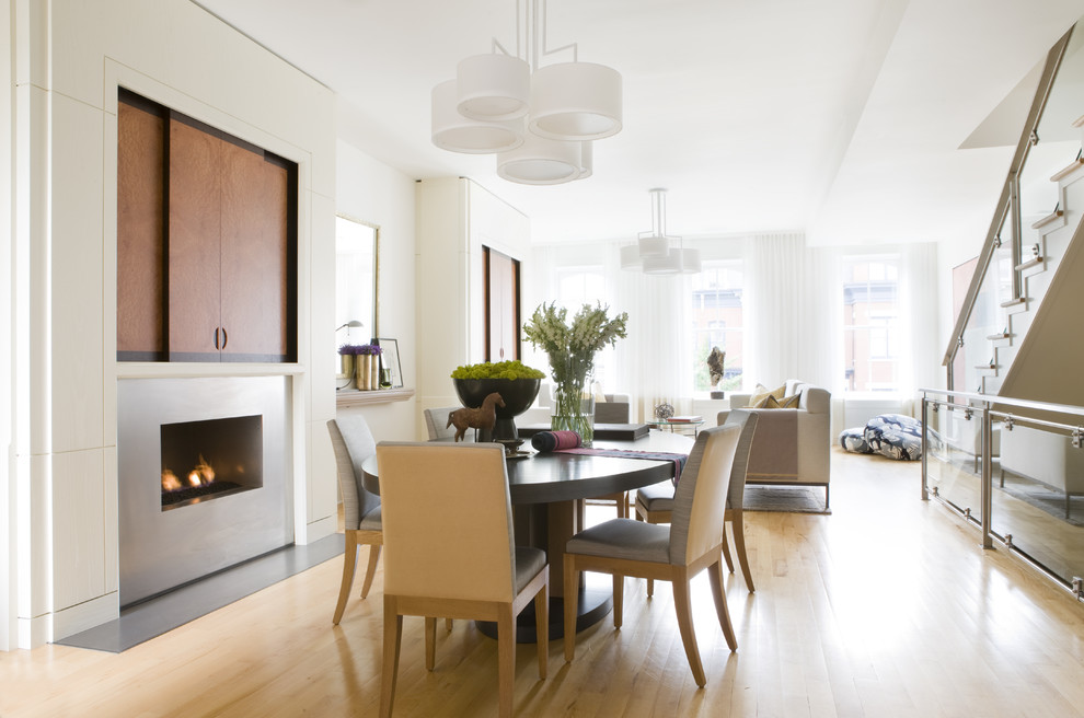 Inspiration for a mid-sized contemporary dining room in DC Metro with beige walls, light hardwood floors, a standard fireplace, a metal fireplace surround and brown floor.