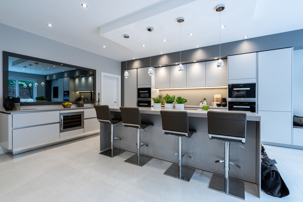 Photo of a large contemporary eat-in kitchen in Hampshire with flat-panel cabinets, grey cabinets, quartz benchtops, grey splashback, stone slab splashback, stainless steel appliances, with island and grey benchtop.