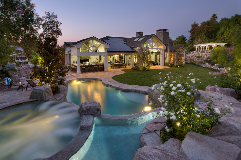 This is an example of a large traditional backyard custom-shaped pool in Orange County with a hot tub and natural stone pavers.