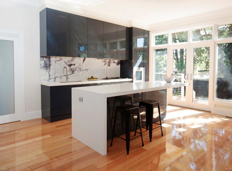 Design ideas for a mid-sized contemporary single-wall open plan kitchen in Melbourne with a double-bowl sink, flat-panel cabinets, black cabinets, quartz benchtops, multi-coloured splashback, marble splashback, stainless steel appliances, medium hardwood floors and with island.