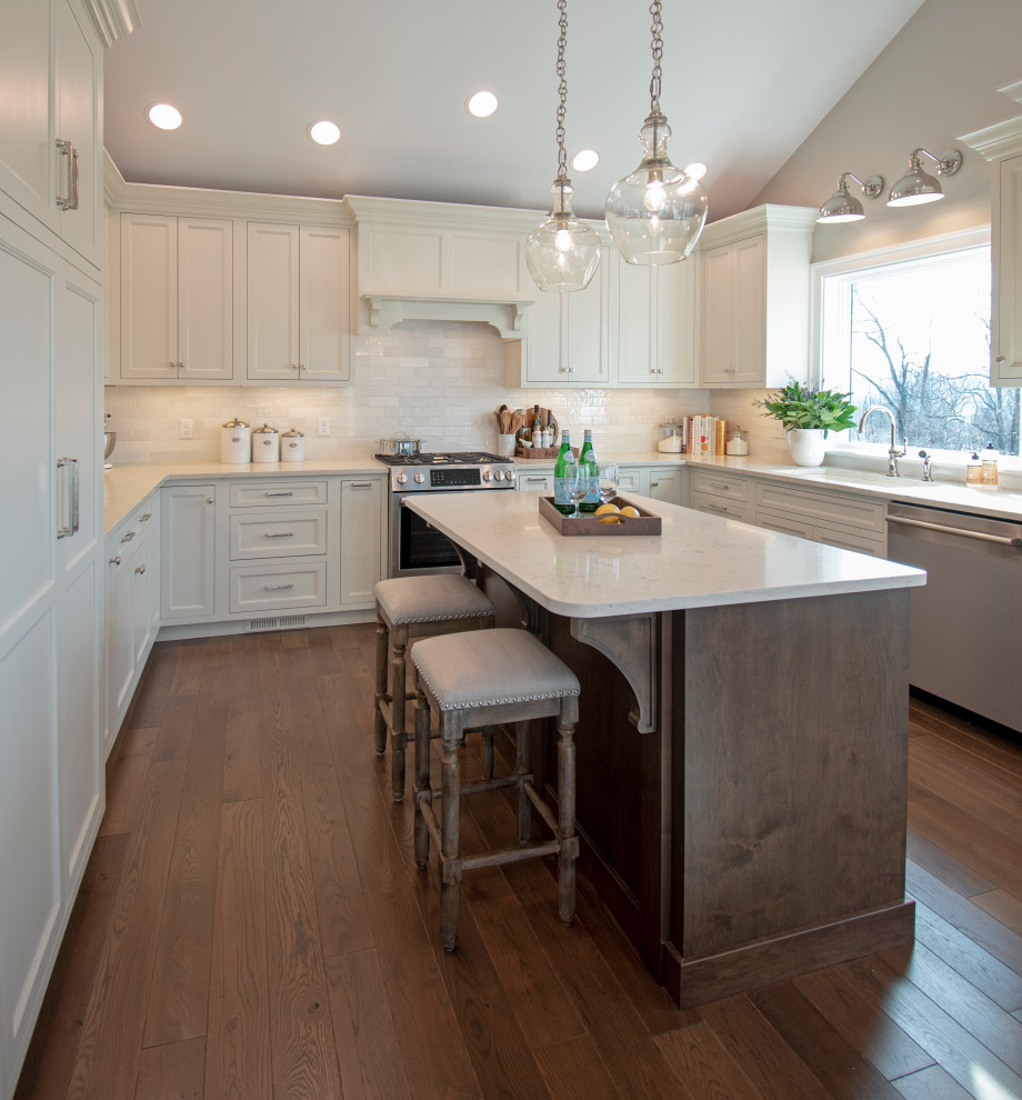 Transitional medium tone wood floor, brown floor and vaulted ceiling eat-in kitchen photo with an undermount sink, shaker cabinets, white cabinets, quartz countertops, white backsplash, ceramic backsplash, stainless steel appliances, an island and white countertops