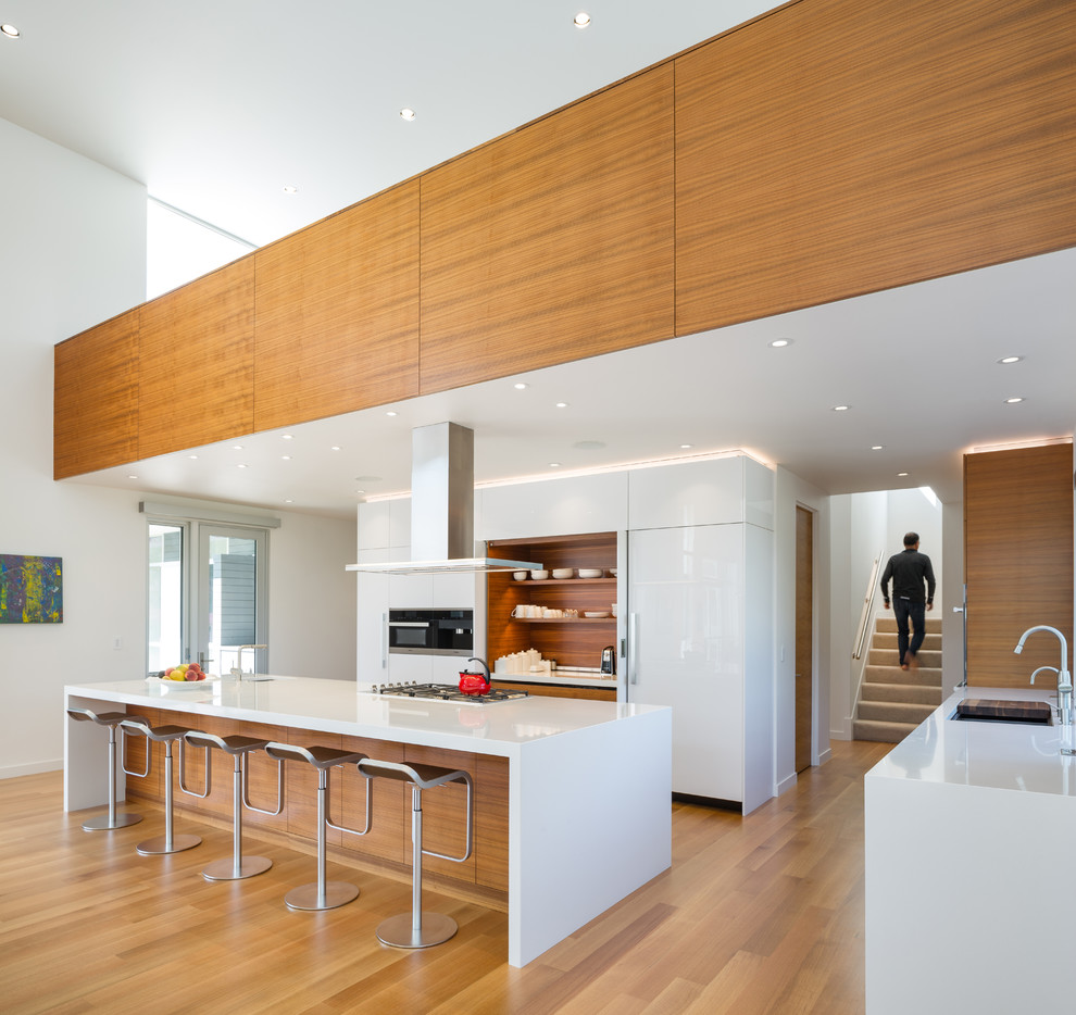 Photo of a modern l-shaped kitchen in Portland with an undermount sink, flat-panel cabinets, white cabinets, panelled appliances, medium hardwood floors, with island, brown floor and white benchtop.