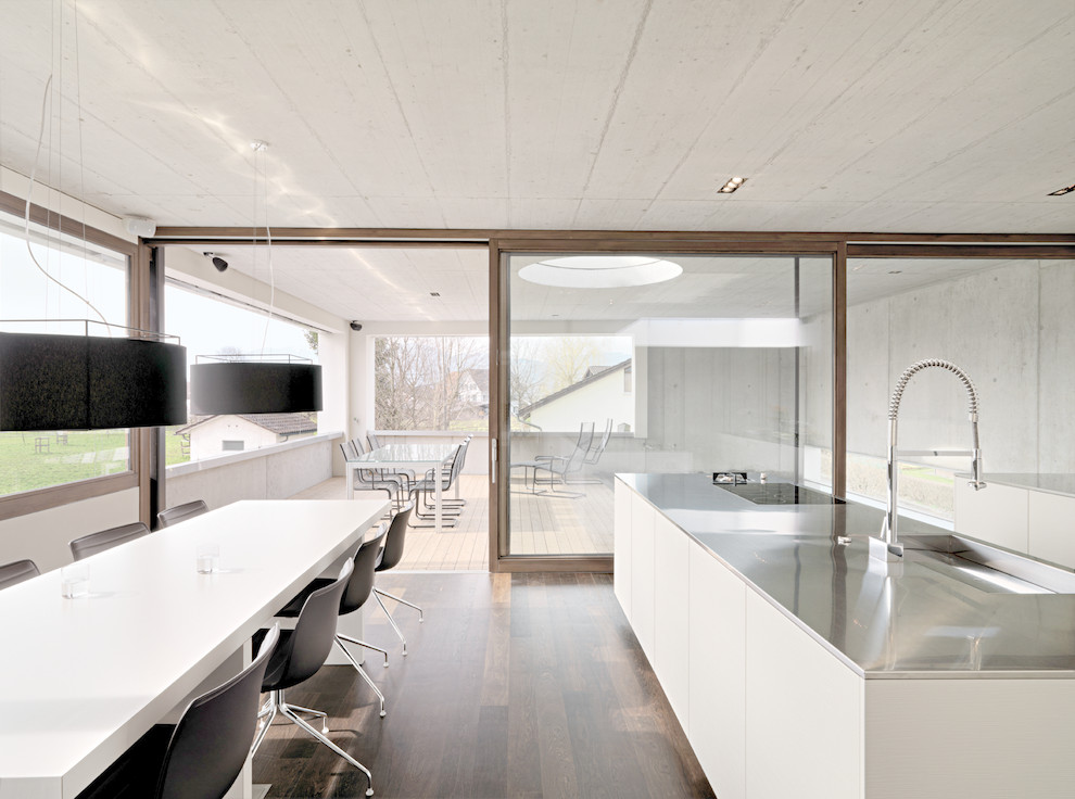 Photo of a large contemporary eat-in kitchen in Stuttgart with an integrated sink, flat-panel cabinets, white cabinets, stainless steel benchtops, dark hardwood floors and multiple islands.