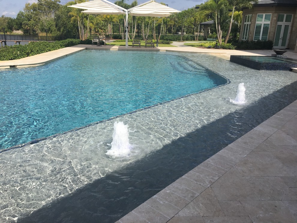 This is an example of an expansive beach style backyard custom-shaped natural pool in Miami with a water slide and natural stone pavers.