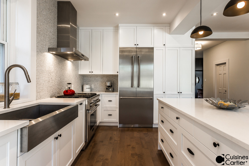 Mid-sized transitional l-shaped medium tone wood floor eat-in kitchen photo in Montreal with a farmhouse sink, shaker cabinets, white cabinets, quartzite countertops, white backsplash, mosaic tile backsplash, stainless steel appliances and an island
