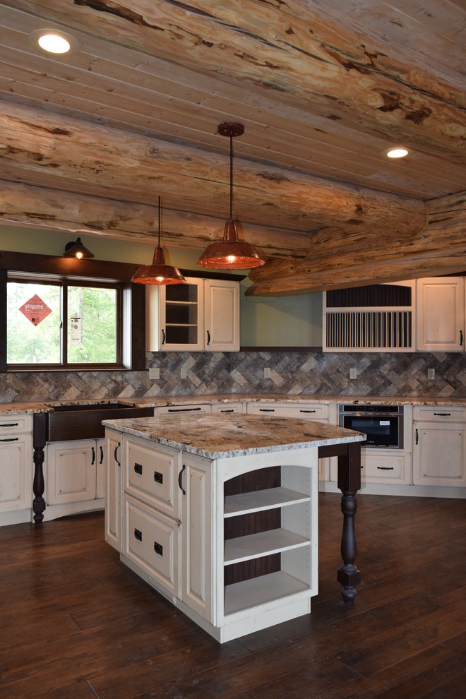 Example of a mountain style u-shaped dark wood floor eat-in kitchen design with a farmhouse sink, raised-panel cabinets, white cabinets, granite countertops, beige backsplash, stone tile backsplash, stainless steel appliances and an island