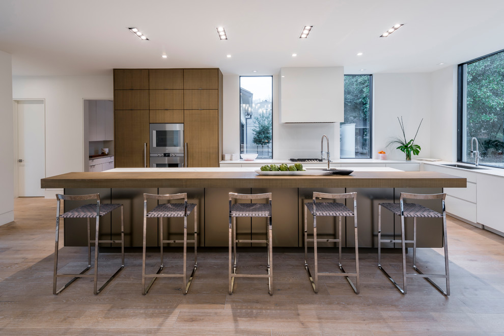 Photo of a mid-sized contemporary single-wall open plan kitchen in Dallas with flat-panel cabinets, stainless steel appliances, medium hardwood floors, with island, brown floor, an undermount sink, brown cabinets, quartz benchtops, white splashback and glass sheet splashback.