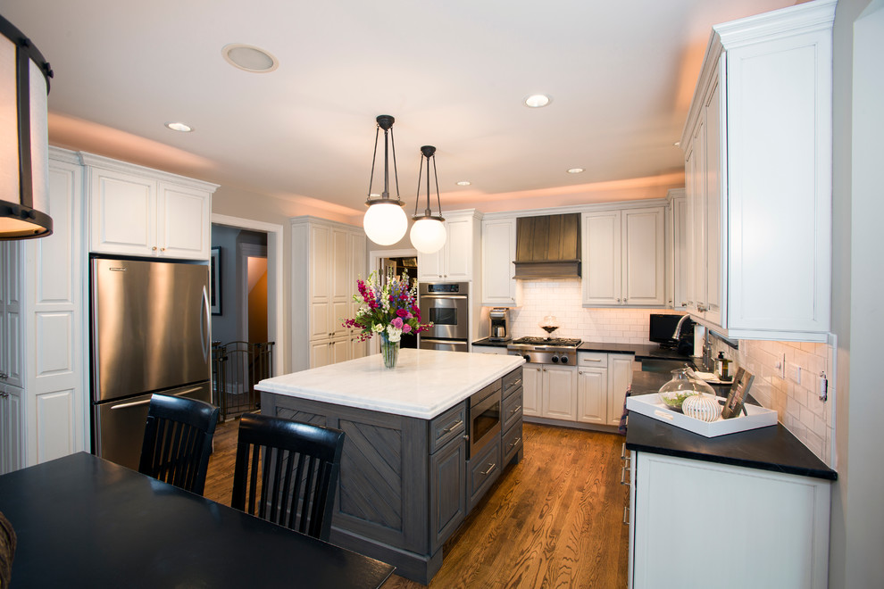 Example of a large transitional u-shaped medium tone wood floor eat-in kitchen design in Chicago with white cabinets, white backsplash, stainless steel appliances and an island