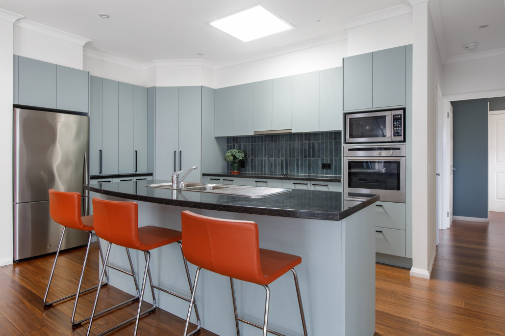 Design ideas for a mid-sized contemporary open plan kitchen in Melbourne with flat-panel cabinets, blue cabinets, quartz benchtops, blue splashback, ceramic splashback, bamboo floors, with island, brown floor and black benchtop.