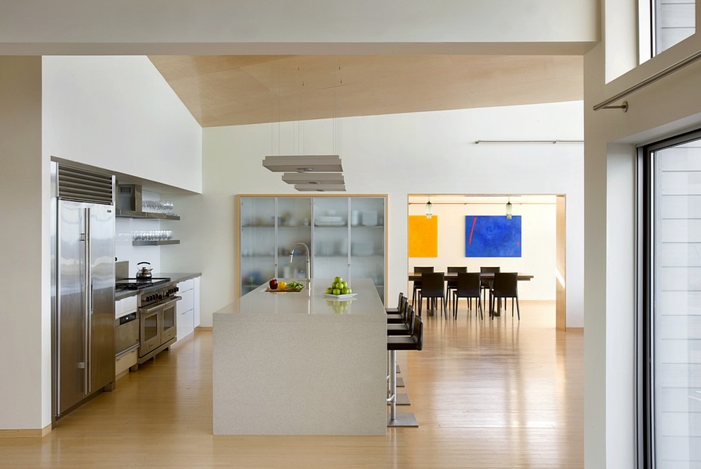 Large modern single-wall open plan kitchen in Boston with an undermount sink, flat-panel cabinets, white cabinets, concrete benchtops, stainless steel appliances, light hardwood floors, with island and beige floor.