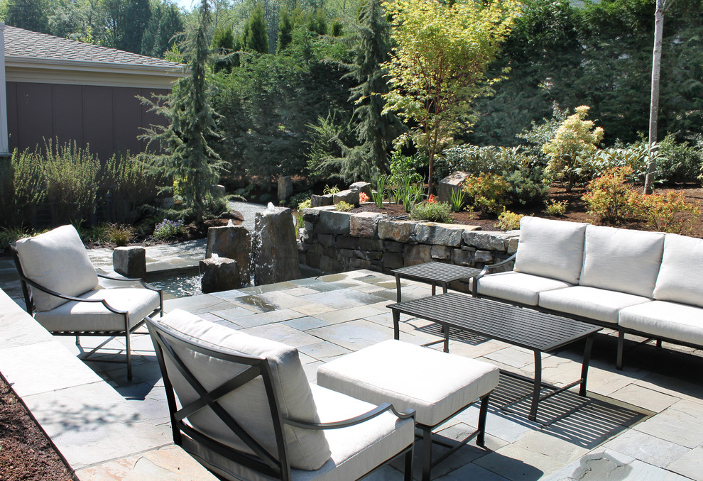 This is an example of a large contemporary patio in Seattle with a water feature, natural stone pavers and no cover.